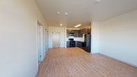This single-floor unit offers a clean, modern aesthetic with a well-considered layout designed for comfortable everyday living. The open-concept living and kitchen area forms the heart of the space, where light hardwood-style flooring extends throughout, creating a warm and cohesive atmosphere. The kitchen is appointed with rich, dark espresso-toned cabinetry providing ample storage, complemented by light countertops and a classic white subway tile backsplash. A full suite of black appliances includes an electric range with overhead microwave, a dishwasher, and a full-size refrigerator, all anchored by a stainless steel sink. The living area is generously proportioned, bathed in natural light from a set of large windows that offer open exterior views, lending an airy, spacious feel to the unit. The bedroom is carpeted for added comfort and warmth, featuring a window for natural light and baseboard heating. The full bathroom is thoughtfully finished with matching dark cabinetry, a white vanity with an integrated sink, and a full shower-tub combination with built-in shelving. The overall design is clean and contemporary, with neutral tones and durable finishes throughout.