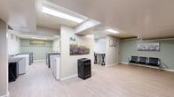 Located at 820 Capital Dr in Carnegie, PA, this community laundry facility offers a practical and well-maintained space designed to accommodate residents with ease. The single-floor layout is thoughtfully organized, encompassing two dedicated laundry rooms and a shared waiting area.

Each laundry room is outfitted with multiple top-loading washers and front-loading washer-dryer units, arranged in parallel rows to maximize efficiency. The rooms feature light wood-look flooring, painted concrete block walls in a soft sage green, and bright overhead fluorescent lighting that ensures excellent visibility. Ventilation is provided through wall-mounted vents, and a utility sink is accessible within the laundry area.

The waiting area provides a comfortable space for residents during their laundry cycles. It is furnished with sleek, black multi-seat benches and includes a work surface for convenience. Decorative wall art adds a welcoming touch, while a vending machine offers refreshments. The waiting area also benefits from a skylight and overhead lighting, creating a bright and pleasant atmosphere. A restroom is accessible directly from this space.

Throughout the facility, the consistent use of light flooring and sage-toned walls creates a cohesive, clean aesthetic. The layout is straightforward and functional, making this laundry facility a reliable and comfortable shared amenity.