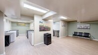 Located at 820 Capital Dr in Carnegie, PA, this community laundry facility offers a practical and well-maintained space designed to accommodate residents with ease. The single-floor layout is thoughtfully organized, encompassing two dedicated laundry rooms and a shared waiting area.

Each laundry room is outfitted with multiple top-loading washers and front-loading washer-dryer units, arranged in parallel rows to maximize efficiency. The rooms feature light wood-look flooring, painted concrete block walls in a soft sage green, and bright overhead fluorescent lighting that ensures excellent visibility. Ventilation is provided through wall-mounted vents, and a utility sink is accessible within the laundry area.

The waiting area provides a comfortable space for residents during their laundry cycles. It is furnished with sleek, black multi-seat benches and includes a work surface for convenience. Decorative wall art adds a welcoming touch, while a vending machine offers refreshments. The waiting area also benefits from a skylight and overhead lighting, creating a bright and pleasant atmosphere. A restroom is accessible directly from this space.

Throughout the facility, the consistent use of light flooring and sage-toned walls creates a cohesive, clean aesthetic. The layout is straightforward and functional, making this laundry facility a reliable and comfortable shared amenity.