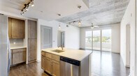 Located at 425 N Boylan Avenue in Raleigh, NC, this 2-bedroom, 2-bathroom residence blends contemporary design with industrial-chic character across a well-appointed single floor. Exposed concrete ceilings and accent walls create a striking visual contrast against crisp white walls and dark hardwood flooring found throughout the main living areas and bedrooms. The open-concept living, dining, and kitchen area is anchored by a central island with a built-in sink, white quartz countertops, and a stainless steel dishwasher. The kitchen is further equipped with warm wood cabinetry, a subway tile backsplash, stainless steel appliances including a range and microwave, and a dedicated pantry. Sliding glass doors lead to a private balcony offering views of the surrounding Raleigh cityscape. Both bedrooms feature concrete accent walls, large windows with city views, and ceiling fans. The primary bedroom connects to a generously sized en suite bathroom with dual sinks, wood vanity cabinetry, tile flooring, and a walk-in closet. The second bathroom mirrors the same refined finishes. A dedicated in-unit laundry room with a full-size washer and dryer adds everyday convenience, while five closets throughout provide ample storage.