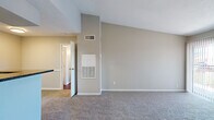 Located at 8380 El Mundo St in Houston, TX, this one-bedroom, two-bathroom unit offers a well-designed single-floor layout. The living room is immediately welcoming, featuring vaulted ceilings that create a sense of openness and volume beyond the unit's footprint, soft carpeting, and a sliding glass door that opens to a private balcony with outdoor views. The adjacent kitchen is efficiently designed with white cabinetry, dark granite countertops, a tile backsplash, and stainless steel appliances including a refrigerator, microwave, and range. A breakfast bar with a built-in sink connects the kitchen to the living area, ideal for casual dining or entertaining. The spacious primary bedroom includes a ceiling fan, plush carpeting, a sliding glass door for additional natural light and balcony access, and leads into a dedicated walk-in closet outfitted with wire shelving and basket storage systems. Both bathrooms are finished with white cabinetry, dark granite vanity tops, and clean white tile. One bathroom features a full tub-shower combination. Rich hardwood-style flooring accents the bathroom areas, providing contrast to the soft carpeting throughout the rest of the unit.