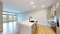 Located at 795 Ironwood Flats Cir in Brandon, Florida, this single-story home offers a clean, contemporary design with an open and airy feel. The heart of the home is the open-concept kitchen and living area, where light wood flooring extends seamlessly throughout the main living spaces, creating a warm and cohesive aesthetic. The kitchen is well-appointed with shaker-style cabinetry in a soft neutral tone, matte black hardware, a white quartz countertop, and a classic subway tile backsplash. A center island with a built-in sink and matte black pull-down faucet serves as both a functional workspace and a natural gathering point. Stainless steel appliances, including a French door refrigerator, electric range, and over-the-range microwave, complete the kitchen's modern look. The adjacent living area is generously proportioned, bathed in natural light from a front-facing window, and features recessed lighting overhead. The bathroom maintains the home's consistent design language with light wood flooring, a white vanity with quartz countertop, matte black fixtures, and a tiled tub-shower combination. Bedroom spaces are carpeted for comfort and finished with neutral walls and clean white baseboards, providing a calm and versatile canvas. Overall, the home presents a fresh, move-in-ready interior with cohesive modern touches throughout.
