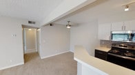 This single-floor residence offers a practical and well-organized layout highlighted by updated finishes throughout. The open-concept living and dining area is anchored by a white brick fireplace and features plush carpeting underfoot. A large sliding glass door floods the space with natural light and provides direct access to an outdoor balcony area, offering views of surrounding greenery. A ceiling fan is positioned overhead in the adjoining area, which connects seamlessly to the kitchen via a peninsula-style breakfast bar with a clean white countertop and dark cabinetry below.

The galley-style kitchen is efficiently designed with ample white upper cabinetry, dark lower cabinets, white quartz countertops, a mosaic tile backsplash, and stainless steel appliances including a refrigerator, microwave, and range. Wood-look flooring and track lighting complete the kitchen's contemporary feel.

The bedrooms are generously sized, each finished with plush carpet, neutral walls, and windows that invite natural light. Multiple bedrooms include dedicated closets with built-in shelving for organized storage. The bathroom features a dark-framed vanity mirror, decorative tile accent wall, white quartz countertop, dark cabinetry, and a tub-shower combination with tile surround. Textured ceilings are consistent throughout the residence.