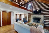 Located at 5036 Hilltop Rd in Greensboro, NC, this character-rich two-story log cabin blends rustic craftsmanship with comfortable living across a generous footprint. The main floor serves as the heart of the home, anchored by a striking stone fireplace in the living room, where original exposed log walls and warm hardwood floors set an inviting, cabin-like atmosphere. Soaring ceilings with visible wooden beams add to the sense of vertical space, complemented by an open loft-style upper level accessible via a wooden staircase with a classic log railing. A secondary living area provides additional lounge space, complete with a game area, making it ideal for gathering. The kitchen features dark cabinetry, stainless steel appliances, and wide-plank hardwood floors, maintaining the home's rustic aesthetic. A dedicated dining area with exposed log walls and vaulted, wood-paneled ceilings adds further charm. The three bedrooms are cozy and well-lit, featuring wood-framed windows and warm neutral tones. A built-in window seat with storage offers a sun-drenched nook with views of the stone exterior. The full bathroom is clean and functional with a tub-shower combination. Throughout, natural light, original log construction, and thoughtful design details define this distinctive Greensboro retreat.