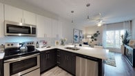 Located at 1840 Rinehart Road in Sanford, Florida, this single-floor residence offers a well-appointed layout with modern finishes and a cohesive contemporary design. The open-concept kitchen is a standout feature, showcasing a striking two-tone cabinet scheme with crisp white upper cabinets and dark wood-grain lower cabinets, complemented by white quartz countertops and a clean tile backsplash. A full suite of stainless steel appliances — including a refrigerator, electric range, over-the-range microwave, and dishwasher — adds both function and style. Sleek pendant lighting and wood-look plank flooring complete the kitchen's polished look, which flows seamlessly into the living area. The bedrooms are comfortably scaled, featuring plush carpeting, ceiling fans, and large windows dressed with light-filtering curtains that invite natural light while maintaining privacy. The neutral, warm tones of the bedroom walls create a calm and restful atmosphere. The bathroom is finished with wood-look tile flooring, a dark vanity with white countertop, and a full soaking tub with shower combination. Throughout the residence, the design emphasizes clean lines, neutral palettes, and modern fixtures, creating a cohesive and inviting living environment suited for everyday comfort.