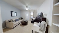 Located at 8439 Dorchester Rd in North Charleston, SC, this single-floor residence offers a thoughtfully designed open-concept layout that seamlessly connects the living, dining, and kitchen areas. The living room features plush carpeting, a ceiling fan, and built-in shelving, creating a comfortable and functional gathering space with natural light filtering in through windows. The open flow leads directly into the dining area and kitchen, which is equipped with warm honey-toned cabinetry, dark granite countertops, a stainless steel double-basin sink, a hanging pot rack, and a kitchen island with bar seating — ideal for both cooking and casual dining. Track lighting adds a practical touch overhead. The primary bedroom is carpeted and features vaulted-style ceilings, soft blue accent walls, a four-poster bed frame, and windows that bring in natural light, accompanied by a walk-in closet. The en-suite bathroom includes granite countertops, a vessel-style sink, tile flooring, and a walk-in shower. Additional bedrooms are carpeted with closet storage and natural light from striped curtained windows. A hallway bathroom with granite countertops completes the home. The neutral color palette and cohesive finishes throughout give the space a clean, welcoming ambiance.