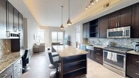Located in the heart of Dallas's vibrant Uptown neighborhood, this thoughtfully designed one-bedroom, one-bathroom residence offers a refined urban living experience across a single well-appointed floor. The open-concept kitchen and living area serves as the heart of the home, showcasing rich dark wood cabinetry, a granite-topped island with seating for multiple bar stools, stainless steel appliances, a decorative tile backsplash, and elegant tray ceilings with ambient lighting. The living room is bright and welcoming, with light hardwood-style flooring, neutral tones, and sliding glass doors that open to a private balcony offering expansive views of the Dallas skyline and surrounding cityscape. The bedroom is a tranquil retreat, comfortably proportioned, with a ceiling fan, natural light from a large sliding glass door, and direct access to the balcony and its sweeping views. The bathroom features a glass-enclosed shower alongside a soaking tub, tile flooring, and a granite vanity with dark cabinetry. A dedicated laundry area houses a stacked full-size washer and dryer, adding everyday convenience. The space is completed by a dedicated closet and entrance foyer, making this residence a functional and sophisticated urban home.