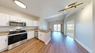 Located at 1 Technology Dr in North Chelmsford, MA, this one-bedroom, one-bathroom residence offers a well-designed single-floor layout with a thoughtful blend of functionality and modern finishes. The open-concept kitchen and living area serves as the heart of the home, featuring vaulted ceilings that lend a sense of spaciousness beyond the unit's footprint. The kitchen is equipped with stainless steel appliances — including a refrigerator, range, microwave, and dishwasher — complemented by white shaker-style cabinetry, granite countertops, and a peninsula with a sink that seamlessly connects to the living area. Rich hardwood-style flooring runs throughout the main living spaces, while sliding glass doors invite abundant natural light and provide direct access to a private patio overlooking lush greenery. The bedroom is finished with plush carpeting, a large window with outdoor views, and generous closet space across three closets. The full bathroom features a soaking tub with tile surround and a white vanity. A dedicated in-unit laundry area adds everyday convenience. Track lighting and clean neutral tones throughout contribute to a bright, contemporary ambiance.
