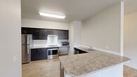 This thoughtfully designed one-bedroom, one-bathroom residence on SW Scholls Ferry Road offers a comfortable and functional single-floor layout. A welcoming entryway with tall ceilings leads into a bright, open living area finished with light wood-style flooring that extends throughout the main living spaces. Large windows and a glass door invite abundant natural light into the living room, which flows seamlessly into the kitchen. The kitchen is a standout feature, showcasing rich dark cabinetry, granite-style countertops, white tile backsplash, and a full suite of stainless steel appliances including a refrigerator, electric range, dishwasher, and microwave. A peninsula counter adds additional prep space and defines the transition between kitchen and living areas. The well-sized bedroom is carpeted for comfort and includes a sliding-door closet with built-in shelving, as well as windows that bring in natural light. A dedicated in-unit laundry closet with a full-size washer and dryer adds everyday convenience. The bathroom features tile flooring, and additional storage is accessible via a linen closet nearby. The neutral color palette and clean finishes throughout create a bright, move-in-ready atmosphere suited for comfortable everyday living.