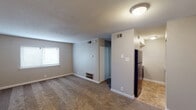 Located at 235 James I Harrison Jr Pkwy E in Tuscaloosa, Alabama, this single-floor unit offers a straightforward and functional layout designed for comfortable everyday living. The spacious living area is finished with wall-to-wall carpeting and neutral gray walls, creating a clean and versatile space. A textured ceiling and flush-mount light fixture provide a classic, understated aesthetic. Natural light filters in through a window fitted with blinds, brightening the open living space. A half-wall partition separates the living area from the kitchen, which features tile flooring, dark cabinetry, white countertops, a black refrigerator, a black electric range with a ventilation hood, and ample overhead storage. The bedroom is generously sized with soft carpet, a window allowing in natural light, and direct access to a walk-in closet. The bathroom is clean and well-appointed, featuring tile flooring, a white vanity with under-sink storage, a mirrored medicine cabinet, a wall-mounted light fixture, and a shower-tub combination. The unit's consistent neutral color palette and practical finishes throughout make it a functional and welcoming space in the heart of Tuscaloosa.
