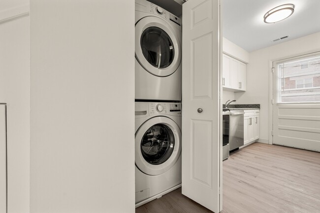 Modern apartment interior with a sleek stackable washer and dryer set in a closet next to a bright kitchen featuring white cabinets - Stony Brook Commons Apartments