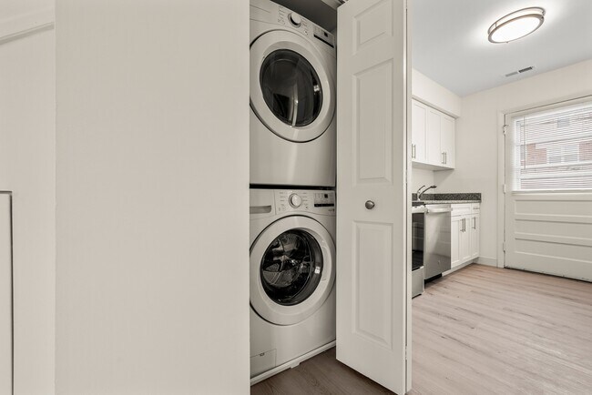 Interior de apartamento moderno con una elegante lavadora y secadora apilables ubicadas en un armario junto a una luminosa cocina con gabinetes blancos. - Stony Brook Commons