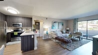 This thoughtfully designed 2-bedroom, 2-bathroom residence offers a functional and stylish single-floor layout. The open-concept living area seamlessly connects the kitchen, dining, and living room, creating a cohesive and welcoming space anchored by wood-look flooring throughout.

The kitchen is a standout feature, boasting dark wood cabinetry extending to the ceiling, stainless steel appliances including a refrigerator, range, and microwave, and a white quartz peninsula countertop that doubles as a breakfast bar. Adjacent to the kitchen, the dining area accommodates a round table and is accented by a decorative mirror wall feature.

The living room is bright and open, benefiting from natural light through a sliding glass door that leads to a private balcony with outdoor views. The two bedrooms are carpeted and well-proportioned, with the primary bedroom offering comfortable dimensions. Both bathrooms are finished with dark wood vanities, white quartz countertops, and full tub-shower combinations with windows that invite natural light. A hallway connects the private quarters and includes laundry access. The consistent neutral color palette and modern finishes throughout create a clean, contemporary ambiance.