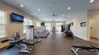 Located at 3500 Pinckney Marsh Ln in Summerville, SC, this fitness center offers a comprehensive workout facility designed to accommodate a wide range of exercise needs. The single-floor layout provides ample open space, with durable rubber flooring throughout that supports both cardio and strength training activities.

The cardio section is well-appointed with multiple treadmills, elliptical machines, and cycling bikes from recognized brands including Life Fitness, Star Trac, and Matrix, allowing users to engage in varied aerobic workouts. Wall-mounted flat-screen TVs are positioned throughout the space to enhance the exercise experience.

The strength training area includes a multi-station cable machine, a variety of selectorized equipment, adjustable benches, a full dumbbell rack, and a complete set of kettlebells and medicine balls on dedicated storage racks. A floor-to-ceiling mirrored wall in the free weights section supports proper form and adds to the sense of openness.

Natural light fills the facility through numerous large windows that frame views of the surrounding greenery. Ceiling fans and recessed lighting contribute to a comfortable and well-lit environment. The neutral color palette of warm gray walls and clean white trim gives the space a modern, welcoming aesthetic suited for daily fitness use.