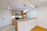 Located in Cambridge, MA, this well-designed one-bedroom, one-bathroom residence with a study offers a functional and comfortable layout across a single floor. The open-concept kitchen flows seamlessly into the combined dining and living area, creating a cohesive and welcoming space. The kitchen is outfitted with warm-toned maple cabinetry, granite countertops, stainless steel appliances including a refrigerator, range, microwave, and dishwasher, and a peninsula with pendant lighting that provides both additional counter space and a natural dividing point between cooking and living areas. Light tile flooring anchors the kitchen zone, while gleaming hardwood floors extend throughout the living and dining space. A triple-panel window in the living area floods the room with natural light and offers views of the surrounding autumn foliage. The bedroom features plush carpeting, a large window with outdoor views, and access to two closets for ample storage. The study, also carpeted, provides a quiet, dedicated space ideal for a home office. The full bathroom is finished with tile flooring, a tub-shower combination, and a wood-tone vanity with a clean white countertop, maintaining the consistent, neutral aesthetic found throughout the residence.