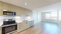 Located in the heart of San Diego's East Village at 1150 E Street, this modern one-bedroom, one-bathroom residence offers a thoughtfully designed open-concept layout across a single floor. Light wood-tone flooring flows seamlessly throughout, complementing the clean, contemporary aesthetic of the space.

The combined kitchen, dining, and living area serves as the heart of the home. The kitchen is outfitted with flat-front light wood cabinetry extending to the ceiling for ample storage, white quartz countertops, a subway tile backsplash, and a full suite of stainless steel appliances including a side-by-side refrigerator, electric range, built-in microwave, and dishwasher.

The bedroom is bright and airy, featuring large floor-to-ceiling windows that frame elevated views of the surrounding San Diego cityscape, filling the room with abundant natural light. A dedicated closet provides organized storage. The bathroom features a floating wood vanity with a gray countertop, a large mirrored medicine cabinet, and marble-style tile flooring, creating a clean and functional space.

Additional highlights include in-unit laundry, a private balcony accessible from the living area, and recessed lighting throughout. The overall ambiance is modern, minimal, and filled with natural light.
