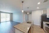 Located at 100 Flint Pond Cir in Shrewsbury, MA, this 2-bedroom, 1-bathroom unit offers a well-designed single-floor layout with a clean, modern aesthetic throughout. The open-concept kitchen and living area serves as the heart of the home, where light wood-style flooring flows seamlessly underfoot. The kitchen is a standout feature, equipped with stainless steel appliances including a refrigerator, electric range, and microwave. Shaker-style cabinetry in a soft gray finish pairs with a granite countertop island that includes an undermount sink, providing generous prep space and casual dining potential. Pendant lighting above the island adds a refined touch. The living room benefits from large sliding glass doors that invite natural light and provide outdoor access. Both bedrooms are comfortably sized — the primary bedroom offering a generous footprint — and each is finished with plush wall-to-wall carpet and neutral gray walls, creating a calm retreat. Windows with blinds bring in natural light while maintaining privacy. The bathroom is outfitted with a full tub-shower combination featuring classic white subway tile surround and chrome fixtures. A dedicated closet provides additional storage. The overall palette of soft grays, whites, and warm wood tones gives the unit a cohesive, contemporary feel.