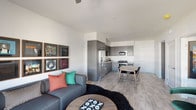 Located at 11126 W Chandler Blvd in Los Angeles, CA, this contemporary single-floor unit showcases a thoughtfully designed open-concept layout with modern finishes throughout. Light wood-tone flooring flows seamlessly across the living, dining, and kitchen areas, creating a cohesive and inviting atmosphere.

The living room is a standout space, featuring a ceiling fan, large windows that allow ample natural light, and a curated gallery wall displaying framed vinyl album covers as a nod to music culture. The room comfortably accommodates a sectional sofa, a media console with a wall-mounted TV, and a statement green accent chair.

The kitchen is well-appointed with dark grey cabinetry, white quartz countertops, a subway tile backsplash, and a full suite of stainless steel appliances including a gas range, built-in microwave, dishwasher, and a French door refrigerator. A dining table with chairs sits adjacent to the kitchen, ideal for everyday meals.

The bedroom offers a dramatic design with bold geometric-patterned wallpaper on the accent wall, flanked by warm wood nightstands and gold-toned lamps. The bathroom features a vanity with a light countertop, a full bathtub with shower, and deep-toned wall finishes that add a moody, sophisticated character to the space.