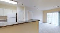 This single-floor residence offers a practical and comfortable layout across two bedrooms and two bathrooms. The kitchen is highlighted by a peninsula with a dark granite countertop, providing additional prep space and a natural divide between the kitchen and the open living area. White cabinetry and a full-size refrigerator contribute to a clean, functional kitchen aesthetic. Neutral cream-toned walls and light carpeting throughout the main living space create a bright, cohesive atmosphere. The open-concept design allows for a seamless transition between the kitchen and the living area, enhancing the overall sense of space. Multiple doorways visible from the main area suggest well-defined bedroom and utility zones while maintaining an accessible, connected feel. Recessed ceiling vents and flush lighting fixtures support a streamlined interior, free of visual clutter. The overall ambiance is clean and understated, offering a neutral backdrop well-suited for a variety of furnishing styles. The two-bathroom configuration adds everyday convenience, making this residence functional for shared or individual living arrangements.