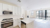 Located at 65-77 Prospect Street in Stamford, Connecticut, this two-bedroom residence offers a clean, modern aesthetic across a thoughtfully arranged single-level floor plan. Light hardwood flooring runs throughout the entire space, complementing the crisp white walls and trim to create a bright, cohesive atmosphere.

A central hallway connects the main living areas and bedrooms, providing a logical and efficient flow throughout the home. The generously sized primary bedroom is bathed in natural light from a large window fitted with horizontal blinds, and includes a dedicated closet, adding practical storage. The second bedroom also features a window with views of the surrounding Stamford streetscape, and benefits from its own wall unit and baseboard heating system.

The living area is open and well-proportioned, with natural light streaming in through windows that frame views of the neighboring cityscape. White walls and high ceilings contribute to an airy, uncluttered feel throughout. The kitchen, visible in the floor plan, features white cabinetry and a marble-style countertop, lending a refined touch to the space.

Clean lines, neutral finishes, and an abundance of natural light define the overall ambiance of this Stamford residence, offering a move-in-ready environment in a convenient downtown location.