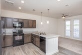 This single-story residence in East Point, Georgia offers a well-designed open-concept layout with distinct zones for living, dining, and cooking. The kitchen serves as a central hub, featuring rich dark wood cabinetry, a tile backsplash, light stone-look countertops, and a full suite of black appliances including a refrigerator, range, microwave, and dishwasher. A peninsula with pendant lighting above creates a natural boundary between the kitchen and the adjoining living area, which is finished with wood-look luxury vinyl plank flooring. The living space is bright and airy, enhanced by a ceiling fan and French doors that open to a private balcony, inviting natural light throughout. Recessed lighting and pendant fixtures provide well-distributed illumination across the main living areas. Bedrooms are finished with plush wall-to-wall carpeting, offering a comfortable, quiet retreat. At least one bedroom includes access to a generously sized walk-in closet outfitted with multi-tiered wire shelving for organized storage. The bathroom features wood-look flooring, dark vanity cabinetry, and a clean walk-in shower with chrome fixtures. Neutral walls and clean architectural lines give the entire unit a move-in-ready, contemporary feel.