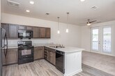 This single-story residence in East Point, Georgia offers a well-designed open-concept layout with distinct zones for living, dining, and cooking. The kitchen serves as a central hub, featuring rich dark wood cabinetry, a tile backsplash, light stone-look countertops, and a full suite of black appliances including a refrigerator, range, microwave, and dishwasher. A peninsula with pendant lighting above creates a natural boundary between the kitchen and the adjoining living area, which is finished with wood-look luxury vinyl plank flooring. The living space is bright and airy, enhanced by a ceiling fan and French doors that open to a private balcony, inviting natural light throughout. Recessed lighting and pendant fixtures provide well-distributed illumination across the main living areas. Bedrooms are finished with plush wall-to-wall carpeting, offering a comfortable, quiet retreat. At least one bedroom includes access to a generously sized walk-in closet outfitted with multi-tiered wire shelving for organized storage. The bathroom features wood-look flooring, dark vanity cabinetry, and a clean walk-in shower with chrome fixtures. Neutral walls and clean architectural lines give the entire unit a move-in-ready, contemporary feel.