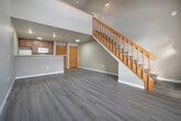 This two-floor residence is designed with a clean, modern aesthetic and a functional open-concept layout. The main level opens into a bright living area finished with light wood-style luxury vinyl flooring that continues throughout the space. A large window fills the living area with natural light, while a prominent wood-railed staircase with open balusters connects the two floors and serves as an architectural focal point.

The kitchen features warm-toned wood cabinetry, white appliances including a refrigerator, range, and over-the-range microwave, and a peninsula with light granite-style countertops. The peninsula separates the kitchen from the living area, creating a natural flow between the two spaces.

The upper level is highlighted by striking vaulted ceilings that dramatically increase the sense of volume in the bedrooms. Each bedroom benefits from the angled roofline and features closet storage, with one room offering a walk-in closet equipped with dual hanging rods and shelving. The bathroom is well-appointed with a full soaking tub and shower combination, a wood-framed vanity with a white countertop, and brushed nickel hardware. Neutral tones are carried throughout the entire residence, contributing to a cohesive and understated overall ambiance.