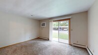 Located at 1016 Lincoln Rd in Bettendorf, Iowa, this single-floor unit offers a practical and straightforward layout designed for comfortable everyday living. The combined kitchen and living room serves as the heart of the space, with the kitchen featuring warm wood cabinetry, dark countertops, white appliances including a range and dishwasher, a ceiling fan with light fixture, and light tile flooring. A pass-through window connects the kitchen to the adjoining area, enhancing the open feel between spaces. The living area is finished with neutral carpet and benefits from a large sliding glass door that fills the room with natural light and provides direct views of the surrounding greenery outdoors. Baseboard heating runs along the walls, and a wall-mounted air conditioning unit ensures year-round comfort. The bathroom is clean and functional, featuring a full-length vanity with an extended countertop, a wide mirror with overhead lighting, a tub-shower combination with tile surround, and light tile flooring. Throughout the unit, warm wood-toned door frames and trim add a consistent finishing touch. The overall aesthetic is understated and practical, offering a move-in-ready space with all essential amenities in a convenient Bettendorf location.