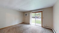 Located at 1016 Lincoln Rd in Bettendorf, Iowa, this single-floor unit offers a practical and straightforward layout designed for comfortable everyday living. The combined kitchen and living room serves as the heart of the space, with the kitchen featuring warm wood cabinetry, dark countertops, white appliances including a range and dishwasher, a ceiling fan with light fixture, and light tile flooring. A pass-through window connects the kitchen to the adjoining area, enhancing the open feel between spaces. The living area is finished with neutral carpet and benefits from a large sliding glass door that fills the room with natural light and provides direct views of the surrounding greenery outdoors. Baseboard heating runs along the walls, and a wall-mounted air conditioning unit ensures year-round comfort. The bathroom is clean and functional, featuring a full-length vanity with an extended countertop, a wide mirror with overhead lighting, a tub-shower combination with tile surround, and light tile flooring. Throughout the unit, warm wood-toned door frames and trim add a consistent finishing touch. The overall aesthetic is understated and practical, offering a move-in-ready space with all essential amenities in a convenient Bettendorf location.