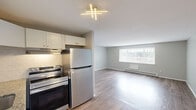 Located at 923 W Main St in New Britain, CT, this 2-bedroom, 1-bathroom unit offers a practical and well-appointed single-floor layout. Throughout the space, light-toned hardwood-style flooring and neutral gray walls create a clean, cohesive aesthetic that lends itself to a variety of interior styles.

The living room is an open, airy space featuring large windows fitted with vertical blinds that allow ample natural light to fill the room. Baseboard heating runs along the walls, and the open sightlines toward the kitchen area provide a connected, functional flow.

Both bedrooms continue the same flooring and neutral palette. The primary bedroom benefits from dual windows that frame outdoor views and provide generous natural light, while a sliding double-door closet offers practical storage. The second bedroom features a single window with a view of the surrounding neighborhood and includes its own closet with a paneled door.

The bathroom is neatly finished with dark slate-style tile surrounding the tub-shower combo, a white vanity with under-cabinet storage, a mirrored medicine cabinet, and contemporary three-bulb vanity lighting overhead — all set against light gray walls and dark tile flooring.

Overall, this unit presents a tidy, move-in-ready space with consistent finishes and efficient use of its compact footprint.