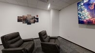 Located at 1908 Fox Rd in Rapid City, South Dakota, this single-room screening and entertainment space is purpose-built for an immersive cinematic experience. The room is finished with clean white walls and a drop tile ceiling with recessed lighting, creating a controlled, theater-like atmosphere. Patterned carpet tiles in a neutral gray tone cover the floor, lending a polished, commercial aesthetic throughout.

The seating area is furnished with multiple dark brown leather recliner chairs arranged in rows, offering comfortable, dedicated viewing positions for every occupant. A large flat-screen display is wall-mounted at the front of the room, serving as the focal point of the space. Cinema-themed wall art — including a multi-panel piece featuring a film reel and clapperboard — reinforces the room's entertainment identity.

Along the back wall, a built-in dark cabinetry unit with a countertop and sink provides a convenient snack and refreshment station, complete with a classic red popcorn machine, adding an authentic movie-theater touch. A solid dark wood door provides access to the adjoining area, and additional multi-panel artwork adorns the side walls. The space is efficiently laid out to maximize seating capacity while maintaining an intimate, focused viewing environment ideal for private screenings or group entertainment.