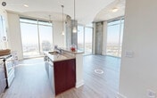 This sophisticated high-rise unit offers a compelling blend of contemporary design and urban living. The open-concept layout is anchored by a well-appointed kitchen featuring rich mahogany cabinetry, stainless steel appliances including a French door refrigerator, a gas range, and a microwave. A central island with a white base provides additional workspace and casual seating, while pendant lighting adds a refined touch overhead.

The living and dining areas are defined by light hardwood-style flooring and dramatic floor-to-ceiling windows that frame sweeping panoramic city views, flooding the space with abundant natural light. Exposed concrete columns lend an industrial character that complements the otherwise clean, minimalist aesthetic. A private balcony extends the living space outdoors, offering an impressive elevated vantage point over the cityscape.

The bedrooms are carpeted for comfort and share the same expansive window treatment, ensuring every room benefits from the stunning views. The hallways feature a distinctive arched ceiling detail, adding architectural interest to the circulation spaces.

Two bathrooms serve the unit, each finished with warm-toned tile flooring, rich wood vanity cabinetry, granite countertops, and large mirrors. One bathroom includes a soaking tub with tile surround. Throughout, the space maintains a cohesive, modern palette of neutral tones and quality finishes.