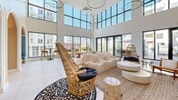 Located at 1340 S Hill St in the heart of Los Angeles, this thoughtfully designed amenity space delivers a compelling blend of contemporary architecture and resort-inspired comfort. The centerpiece is a soaring double-height lounge bathed in natural light through expansive floor-to-ceiling windows, offering sweeping views of the surrounding Downtown LA skyline. Dramatic circular chandeliers cascade from the ceiling above a curated seating arrangement of plush sofas, woven rattan chairs, and game tables, all set atop large-format tile flooring.

A series of elegant arched doorways connects the main lounge to a series of intimate private nooks upholstered in rich teal velvet, providing quieter spaces for conversation or relaxation. Adjacent to these is a full kitchen and bar area, complete with stainless steel appliances, a chevron-patterned accent wall, a central island with polished countertops, and stylish bar seating.

The hallways are defined by a clean, modern aesthetic, featuring the same arched architectural detailing and a long service counter with integrated storage. The outdoor areas are equally impressive, with two resort-style swimming pools surrounded by checkered pool decks, lounge chairs with umbrellas, pergola shading structures, and glass-railed terraces overlooking the vibrant South Hill Street corridor.