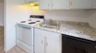Located at 52 Perry Hill Rd in Ashford, Connecticut, this two-floor residence offers a straightforward and functional layout across its two levels. The main floor features a generously sized living area finished with warm hardwood flooring, seamlessly connected to an entry foyer with staircase access to the upper level. The kitchen is equipped with white cabinetry accented by gold-tone hardware, granite-style countertops, a stainless steel sink, an electric range, and a dishwasher. A window above the counter brings in natural light and offers an outdoor view of the surrounding greenery. The main floor also includes a half bath tucked beneath the staircase, featuring tile flooring and a compact, efficient layout. Upstairs, the bedrooms are carpeted for comfort, with one featuring a sliding double-door closet. The upper level also includes a full bathroom with a tub-shower combination set against tiled walls, as well as a second bathroom with a white vanity, mirror, and tile flooring. Baseboard heating is present throughout both floors. The clean, neutral palette of white walls across the entire home provides a bright and move-in ready environment with ample opportunity for personalization.
