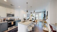 Located at 1440 Yellow Desert Way in Wendell, NC, this single-floor, 3-bedroom, 2-bathroom home offers a well-designed open-concept layout that maximizes comfort and functionality. The kitchen is a standout feature, showcasing a large granite-topped island with an undermount sink and seating, two-tone cabinetry with crisp white uppers and slate-blue lowers, stainless steel appliances including a french door refrigerator, and sleek pendant lighting overhead. The kitchen flows seamlessly into the living area, which is bathed in natural light from large windows and a glass door that opens to a private balcony — perfect for enjoying outdoor views. Hardwood-style flooring runs throughout the main living areas, complemented by a ceiling fan and recessed lighting. The primary bedroom is a comfortable retreat, featuring windows on two walls, a ceiling fan, and access to a private en-suite bathroom with a dual-sink granite vanity, white cabinetry, and a glass-enclosed shower. A spacious walk-in closet with built-in wire shelving provides ample storage. The additional bedrooms are bright and well-proportioned. The second bathroom features a tub-shower combination and hardwood-style floors. Three connecting hallways ensure a smooth flow throughout the home.