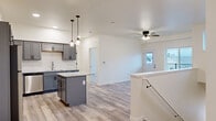 This 3-bedroom, 2-bathroom home offers a clean, modern aesthetic with a well-planned layout that maximizes functionality. The open-concept kitchen and living area serves as the heart of the home, featuring gray shaker-style cabinetry, a center island with light granite countertops, pendant lighting, and a full suite of stainless steel appliances. Light wood-tone luxury vinyl plank flooring extends throughout the main living areas, complemented by crisp white walls and ceiling fans that enhance the bright, airy atmosphere. The living room benefits from natural light through large windows and a glass-panel door that opens to an outdoor balcony area with exterior views.

The three bedrooms are carpeted for comfort, each offering ceiling fans, windows with natural light, and outdoor views. The primary bedroom includes access to a dedicated closet with wire shelving systems, providing generous storage. The two bathrooms are finished with gray vanities, light stone countertops, wood-look tile flooring, and tub-shower combinations with clean white surrounds.

A dedicated laundry room houses a full-size washer and dryer, while three closets throughout ensure ample storage. A carpeted staircase with a white handrail adds a clean, polished transition within the home. Overall, the space presents a cohesive, move-in-ready interior with contemporary details throughout.