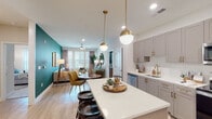 This thoughtfully designed single-floor residence offers a seamless blend of modern aesthetics and functional living. The open-concept layout connects the kitchen, dining, and living areas into a cohesive, inviting space. The kitchen is outfitted with grey shaker-style cabinetry accented by brushed gold hardware, white quartz countertops, a subway tile backsplash, stainless steel appliances, and a spacious island with bar seating. Globe pendant lights with gold fixtures add a warm, contemporary touch overhead. The living area features a bold teal accent wall, light hardwood flooring, and large windows that welcome abundant natural light, with a ceiling fan completing the comfortable atmosphere. The dining area sits naturally between the kitchen and living space, ideal for everyday use and entertaining. Each bedroom is carpeted for comfort and includes ceiling fans, generous windows with exterior views, and thoughtfully appointed details. The primary bathroom impresses with marble-style tile flooring, a soaking tub and shower combo, a wide vanity with wood cabinetry, quartz counters, and a large framed mirror. A secondary bathroom echoes the same refined finishes. Throughout, the space maintains a cohesive palette of warm neutrals, natural wood tones, and gold accents, creating a polished and welcoming ambiance.