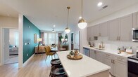 This thoughtfully designed single-floor residence offers a seamless blend of modern aesthetics and functional living. The open-concept layout connects the kitchen, dining, and living areas into a cohesive, inviting space. The kitchen is outfitted with grey shaker-style cabinetry accented by brushed gold hardware, white quartz countertops, a subway tile backsplash, stainless steel appliances, and a spacious island with bar seating. Globe pendant lights with gold fixtures add a warm, contemporary touch overhead. The living area features a bold teal accent wall, light hardwood flooring, and large windows that welcome abundant natural light, with a ceiling fan completing the comfortable atmosphere. The dining area sits naturally between the kitchen and living space, ideal for everyday use and entertaining. Each bedroom is carpeted for comfort and includes ceiling fans, generous windows with exterior views, and thoughtfully appointed details. The primary bathroom impresses with marble-style tile flooring, a soaking tub and shower combo, a wide vanity with wood cabinetry, quartz counters, and a large framed mirror. A secondary bathroom echoes the same refined finishes. Throughout, the space maintains a cohesive palette of warm neutrals, natural wood tones, and gold accents, creating a polished and welcoming ambiance.