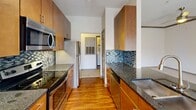 Located at 4915 Misty Oaks Dr in Charlotte, NC, this one-bedroom, one-bathroom residence offers a well-organized single-floor layout that makes efficient use of its space. The open-concept kitchen and living area serve as the heart of the home, with the kitchen showcasing warm wood cabinetry, dark granite countertops, a mosaic tile backsplash, and a full suite of stainless steel appliances including a range, built-in microwave, and refrigerator. Track lighting overhead adds a modern touch, while hardwood-style flooring grounds the kitchen's contemporary aesthetic. The living area transitions seamlessly via plush carpeting and features sliding glass doors and large windows that flood the room with natural light and provide outdoor views. Crown molding adds a refined architectural detail to the living space. The bedroom is a comfortable retreat with soft carpet, a ceiling fan, and a window overlooking the outdoors. The bathroom is well-appointed with a dual-sink vanity topped with granite, warm wood cabinetry, and a large mirror with stylish bar lighting. A dedicated laundry area with a full-size washer and dryer adds everyday convenience, completing this thoughtfully designed Charlotte residence.