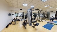Located at 80 St Clair Ave E in midtown Toronto, this fitness facility offers a comprehensive workout environment within a compact, efficiently organized single-room layout. The space features light hardwood-style flooring throughout, a dropped ceiling with recessed panel lighting that ensures bright, even illumination, and a full-wall mirror that visually expands the room and allows users to monitor their form during exercise.

The facility is well-stocked with a diverse range of equipment to support both cardiovascular and strength training. Cardio offerings include elliptical trainers and a stationary bike, while the strength training area is anchored by a multi-station Precor cable machine, a pull-up and dip tower, and a dedicated free weights section featuring dumbbells, a weight bench, and barbells. Yoga mats, resistance bands, and medicine balls are also available for flexibility and functional training.

A water cooler provides convenient in-room hydration, and the space is monitored by a security camera for user safety. Clearly marked exit signage and a glass-paneled entry door contribute to a safe and accessible environment. The mirrored wall not only enhances the sense of openness but also serves as a practical training aid. Overall, this fitness room delivers a thorough and functional workout experience in a clean, well-maintained setting.