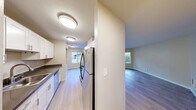 Located at 3030 NE 143rd St. in Seattle's Lake City neighborhood, this two-bedroom, two-bathroom residence offers a well-designed single-level layout. The living room is a bright, open space featuring light hardwood-style flooring, large windows, and a sliding glass door that opens to a private balcony with outdoor views — allowing natural light to fill the room throughout the day. The galley-style kitchen is efficiently designed with white shaker cabinetry, dark countertops, stainless steel appliances including a refrigerator, range, and dishwasher, and light wood-style flooring that carries through from the living area. The two bedrooms are carpeted for comfort, with the generously sized primary bedroom offering ample space for a full furniture arrangement. Both bathrooms are finished with white vanity cabinetry, dark countertops, large mirrors, and brushed nickel fixtures, maintaining a clean and consistent aesthetic. A dedicated closet provides additional storage. The neutral warm-toned walls and consistent finishes throughout give the home a cohesive, move-in-ready feel. A well-rounded layout designed for comfortable everyday living in Seattle.