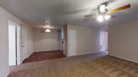This single-floor unit offers a practical and functional layout connecting several distinct living spaces. The main living area is generously sized, featuring neutral beige walls, a textured ceiling, and a ceiling fan with integrated lighting. Carpet covers the living area floors, transitioning to wood-style flooring in the adjoining dining and kitchen zones. A sliding glass door fitted with vertical blinds admits natural light and provides exterior access.

The kitchen is efficiently arranged with white cabinetry, dark granite-style countertops, a white electric coil range with overhead ventilation, and a standard sink. Ample cabinet storage lines the walls, keeping the space organized.

The bedrooms continue the carpeted flooring and neutral color palette, each featuring a ceiling fan, window with blinds for natural light, and access to closet space. The textured ceilings carry throughout the unit, maintaining a consistent aesthetic.

The bathrooms are equipped with white cabinetry topped with dark countertops, tub-shower combinations with white tile surrounds, and wood-style flooring. The overall ambiance of the unit is clean and straightforward, offering a comfortable and move-in-ready environment.