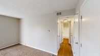 This single-floor residence offers a clean, functional layout with a neutral color palette that creates a bright and welcoming atmosphere throughout. The main living area features warm hardwood flooring and a ceiling fan, with vertical blinds providing light control and privacy. The kitchen is equipped with dark espresso cabinetry, granite-style countertops, a black electric range with overhead ventilation, and hardwood flooring that continues from the adjoining spaces. A connecting hallway links the main living areas to the private quarters, transitioning from hardwood to plush carpeting in the bedrooms. The bedrooms are spacious and bright, each featuring louvered closet doors and ample natural light from well-placed windows with views of the surrounding neighborhood. The bathroom is outfitted with a wide vanity, large mirror, brushed nickel fixtures, and a well-lit vanity light bar. Textured ceilings are consistent throughout the unit, and the HVAC system features ceiling vents for efficient climate control. The overall layout, as seen in the dollhouse view, is open and well-proportioned, offering a comfortable and practical living environment.