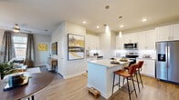 This single-floor residence is thoughtfully designed with a contemporary aesthetic, combining clean lines, neutral tones, and quality finishes throughout. An entry hallway leads into the heart of the home, where the kitchen and living areas flow seamlessly together in an open-concept layout. The kitchen is a standout feature, equipped with white shaker-style cabinetry extending to the ceiling, granite countertops, a subway tile backsplash, and a full suite of stainless steel appliances including a side-by-side refrigerator, electric range, and over-the-range microwave. A central island with granite countertop and bar seating serves as both a functional workspace and a casual dining spot, illuminated by sleek pendant lighting above. Light wood-style flooring runs throughout the main living areas, contributing to a warm, cohesive feel. The living room offers generous space, large windows that invite natural light, and a ceiling fan overhead. The bedrooms are carpeted for comfort, with the primary bedroom featuring multiple large windows framing outdoor views. Bathrooms are finished with granite-topped white vanities, wood-style flooring, and a soaking tub with a tiled surround, providing a clean, spa-like atmosphere.