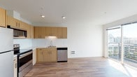Located at 429 2nd Avenue West in Seattle's Queen Anne neighborhood, this single-floor residence offers a thoughtfully designed open-concept layout with clean, contemporary finishes throughout. Warm wood-tone luxury vinyl plank flooring runs continuously across the living, kitchen, and bedroom areas, creating a cohesive and inviting atmosphere.

The kitchen is a standout feature, outfitted with flat-front, light wood cabinetry offering generous upper and lower storage. Stainless steel appliances include a full-size refrigerator, electric range, built-in microwave, and dishwasher. A white quartz countertop and textured white tile backsplash complete the polished look, while recessed lighting ensures the space is well-illuminated.

The open living area flows naturally from the kitchen, benefiting from natural light through a sliding glass door that leads to an outdoor balcony. The bedroom is a calm, well-proportioned space with neutral white walls and consistent flooring, offering a versatile canvas for personalization.

The bathroom features a wood-tone vanity with a white quartz countertop, an undermount sink, and a large mirror, all set against bright white walls and matching wood-look flooring. The overall design emphasizes simplicity, functionality, and modern aesthetics throughout.