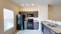 This single-story unit at Windhurst Park offers a thoughtfully designed layout with a clean, modern aesthetic throughout. The kitchen serves as a functional centerpiece, showcasing rich dark-stained cabinetry that extends to the upper walls, providing generous storage space. Speckled granite-style countertops run along the perimeter, complementing the full suite of black appliances, which includes a refrigerator, electric range, over-the-range microwave, and dishwasher. Recessed lighting illuminates the space from above, while light-toned wood-style flooring adds a contemporary finish underfoot.

The bathroom maintains a neutral, understated palette with warm beige walls and earthy stone-patterned tile flooring. It features a standard tub-shower combination, a toilet, and a vanity with matching granite-style countertop, all accented by recessed overhead lighting for a clean, practical finish.

The bedroom is carpeted in a medium-toned plush carpet, creating a comfortable, quiet atmosphere. A window fitted with horizontal blinds allows natural light to filter in, while a ceiling fan with an integrated light fixture provides both ventilation and additional illumination. Neutral walls and clean white baseboards contribute to the unit's cohesive, move-in-ready feel.
