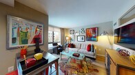This single-floor unit offers a thoughtfully designed layout that balances functionality with a bold, artistic aesthetic. Throughout the space, warm-toned hardwood-style flooring, neutral taupe walls, and recessed lighting create a cohesive and inviting atmosphere.

The living area is bright and generously proportioned, benefiting from large windows that frame urban views and flood the room with natural light. Bold artwork and vibrant accents punctuate the neutral backdrop, lending the space a dynamic, energetic character.

The kitchen is well-appointed with rich cherry wood cabinetry, a slate-toned subway tile backsplash, light countertops, and a full suite of stainless steel appliances including a refrigerator, range, microwave, and dishwasher. A dedicated in-unit laundry closet adds convenience.

The bedroom is a quieter retreat, featuring carpet flooring, a horizontal window, and warm, understated décor. The full bathroom is finished with large-format tile flooring, a warm wood vanity, white countertops, and a tub-shower combination.

A hallway adorned with vibrant abstract artwork connects the rooms, reinforcing the unit's spirited, gallery-like character throughout.