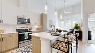 This thoughtfully designed 1-bedroom, 1-bathroom residence showcases a modern aesthetic with an open-concept layout that maximizes every inch of its single-floor footprint. Dramatic soaring ceilings in the kitchen and living area create an airy, expansive atmosphere that far exceeds the sense of its physical dimensions.

The kitchen is a standout feature, equipped with stainless steel appliances including a range, microwave, and refrigerator. Two-tone cabinetry pairs crisp white upper cabinets with warm wood-finish lower cabinets, complemented by a marble-style backsplash and light quartz countertops. A central island with seating provides both additional prep space and a casual dining option. Elegant pendant lighting hangs above, adding a refined touch.

The living area flows naturally from the kitchen, bathed in natural light from large windows that offer outdoor views. Light hardwood-style flooring runs throughout the main living spaces, adding warmth and continuity.

The bedroom is a comfortable retreat featuring plush carpeting, large windows with ample natural light, and generous space for furnishings. A dedicated laundry area houses a full-size stacked washer and dryer with built-in shelving nearby. The bathroom and hallway maintain the clean, neutral palette consistent throughout the residence, creating a cohesive and polished living environment.