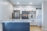 This efficiently designed single-floor studio in Memphis, TN offers a well-appointed layout that maximizes every square foot. Light hardwood flooring runs throughout the main living area, complementing the neutral, warm-toned walls and recessed lighting that keep the space feeling bright and open.

The kitchen serves as a standout feature, anchored by a bold navy blue island topped with a striking marble-veined countertop. White shaker cabinets line the walls alongside a matching marble backsplash, and stainless steel appliances — including a gas range, microwave, and refrigerator — complete the setup. A stacked washer and dryer unit is conveniently integrated into the kitchen area.

The living space includes a wall-mounted HVAC unit and a window offering natural light. Two built-in closets with wire shelving and a built-in bench provide generous storage for a studio-sized unit.

The bathroom features black hexagonal tile flooring, a walk-in glass-enclosed shower, a wood-toned vanity, and a round mirror, creating a clean, contemporary aesthetic. Recessed lighting and modern black fixtures add refined finishing touches throughout the space.