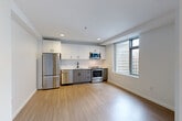 Located at 250 Kendall St in Cambridge's vibrant Kendall Square neighborhood, this modern studio offers a thoughtfully designed open-plan layout that efficiently combines the living, dining, and kitchen areas into one cohesive space. Light hardwood-style flooring flows throughout, complementing the clean white walls and recessed lighting that keep the interior bright and airy.

The kitchen is well-appointed with sleek two-tone cabinetry — white upper cabinets paired with gray lower cabinets — set against a light tile backsplash. A full suite of stainless steel appliances includes a refrigerator, dishwasher, range, and over-range microwave, along with a black-finish sink and faucet. Large windows allow generous natural light into the kitchen and living area, framing views of the surrounding urban landscape.

The bathroom is a standout feature, offering a glass-enclosed shower stall, a modern gray floating vanity with an undermount sink and matte black faucet, and a bright window that enhances the clean, spa-like atmosphere. An in-unit washer is conveniently integrated into the bathroom space. A dedicated closet provides additional storage, completing this efficient and stylish urban unit.